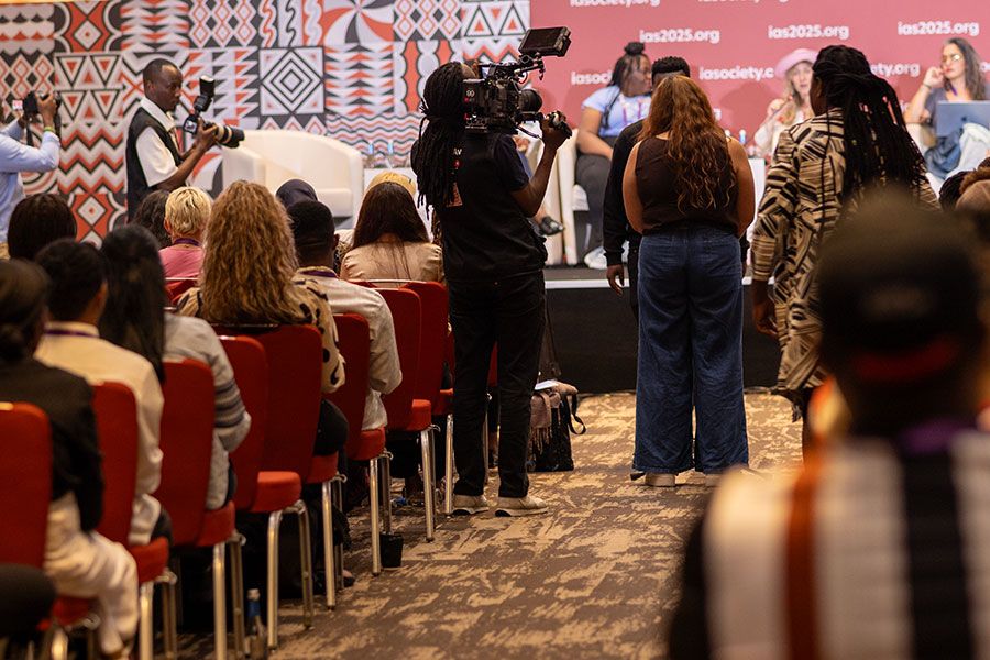 Videographer filming a conference panel discussion audience seated in red chairs at the IAS 2025 event.