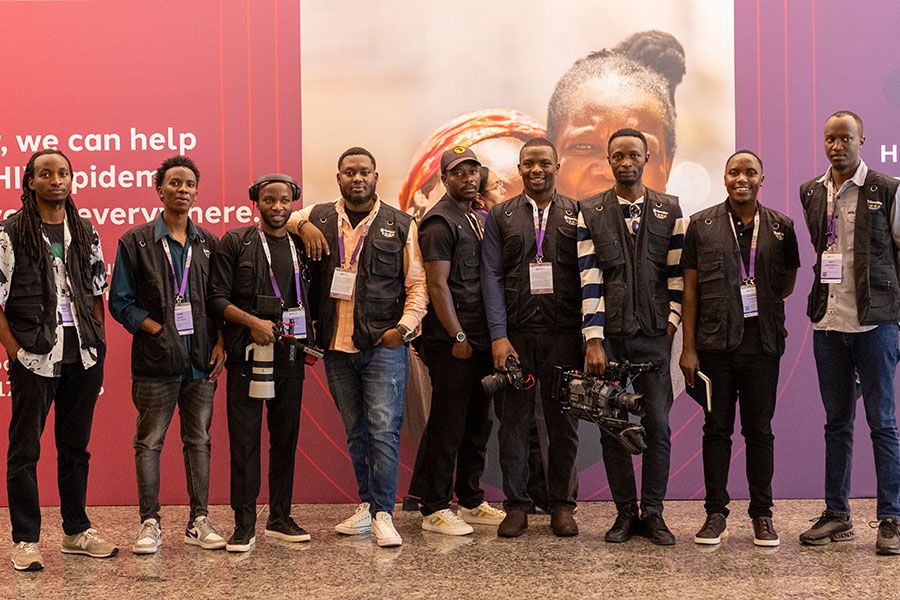 A team of professional event photographers and videographers in black vests posing with cameras in front of a purple banner.