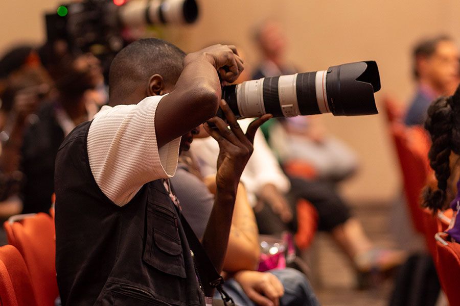 A professional photographer capturing a corporate event with a DSLR camera and telephoto lens.