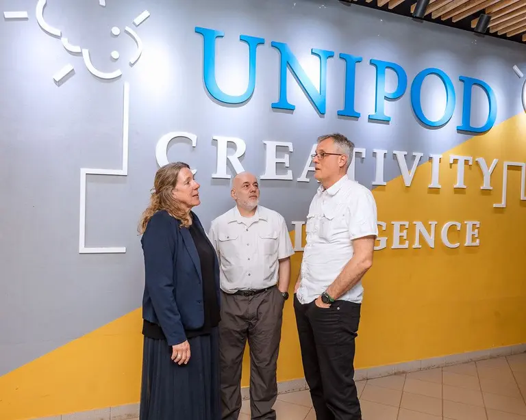 Three professionals discuss innovation in front of a blue and white UNIPOD Creativity wall mural during a project meeting.