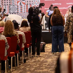 Videographer filming a conference panel discussion audience seated in red chairs at the IAS 2025 event.