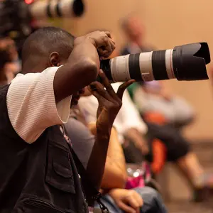 A professional photographer capturing a corporate event with a DSLR camera and telephoto lens.